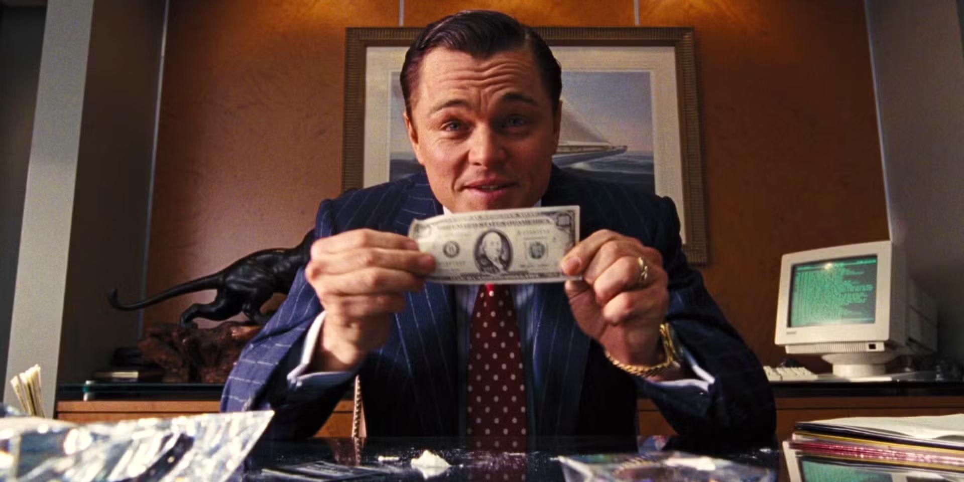 لئوناردو دی کاپریو یک اسکناس 100 دلاری را جلوی دوربین در The Wolf of Wall Street بالا گرفته است - کودکان و The Wolf of Wall Street