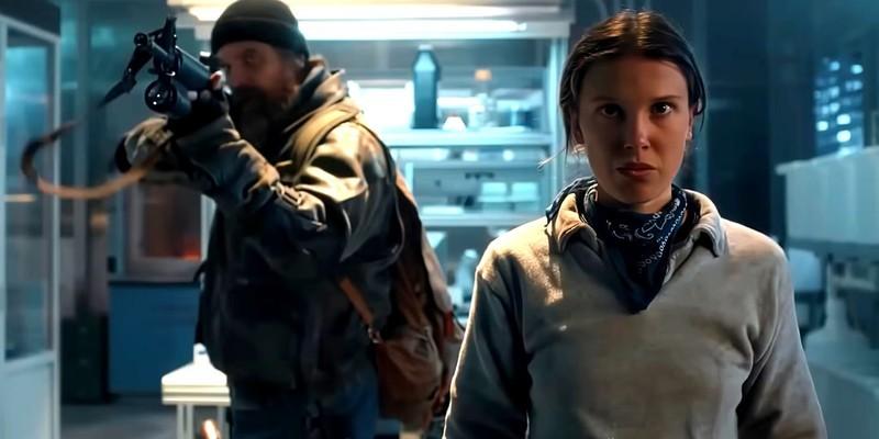 اِلِوِن (Eleven) با بازی میلی بابی براون (Millie Bobby Brown) با چهره ای مصمم در حالی که هاپر (Hopper) با بازی دیوید هاربور (David Harbour) پشت سرش با یک شات گان ایستاده در فصل 5 Stranger Things – انتشار سریع فصل جدید سریال