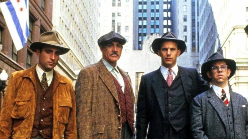 اعضای گروه The Untouchables در فیلم The Untouchables، از فیلم های غیر وسترن کوین کاستنر، در خیابان ایستاده و تماشا می کنند.