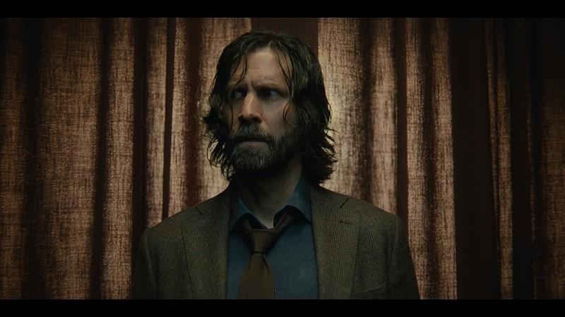 اسکرین شات Alan Wake 2 که آلن را در لباس لایو اکشن در مقابل پرده صحنه نشان می دهد