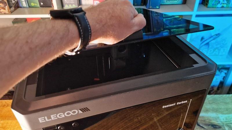 دستی در حال بلند کردن درِ Elegoo Centauri Carbon برای ساخت Catan با پرینتر سه بعدی