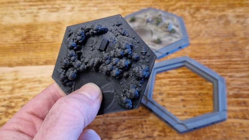 دستی که یک کاشی جنگلی پرینت شده سه بعدی Catan را نگه داشته است، نمونه ای از ساخت Catan با پرینتر سه بعدی