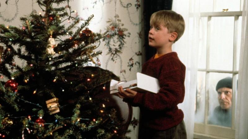 کوین مک آلیستر در حال تزئین درخت کریسمس در حالی که یک دزد خیس از پنجره اش در Home Alone نگاه می کند - تست فیلم کریسمس