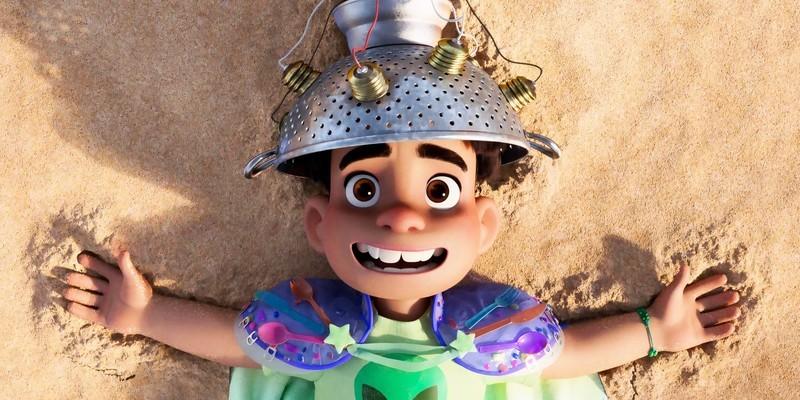 Elio lays on the sand and smiles with a strainer on his head