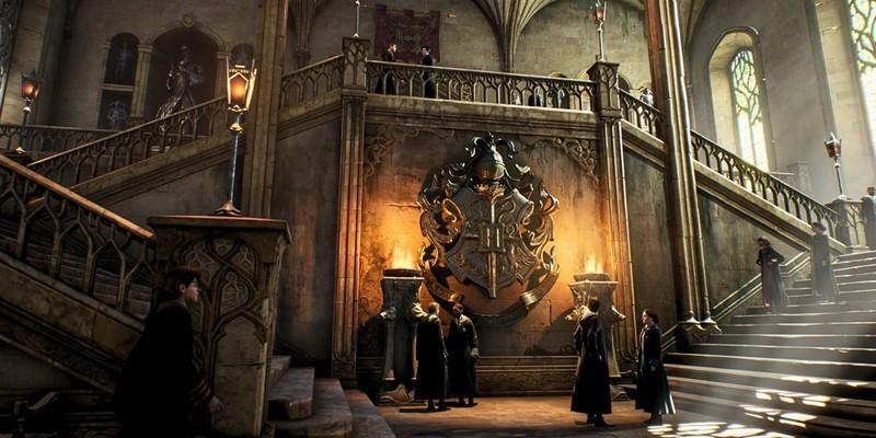 دانش آموزانی که در Hogwarts Legacy جلوی نشان مدرسه در پایین پله های هاگوارتز جمع شده اند (1) و منتظر Hogwarts Legacy DLC رایگان هستند.