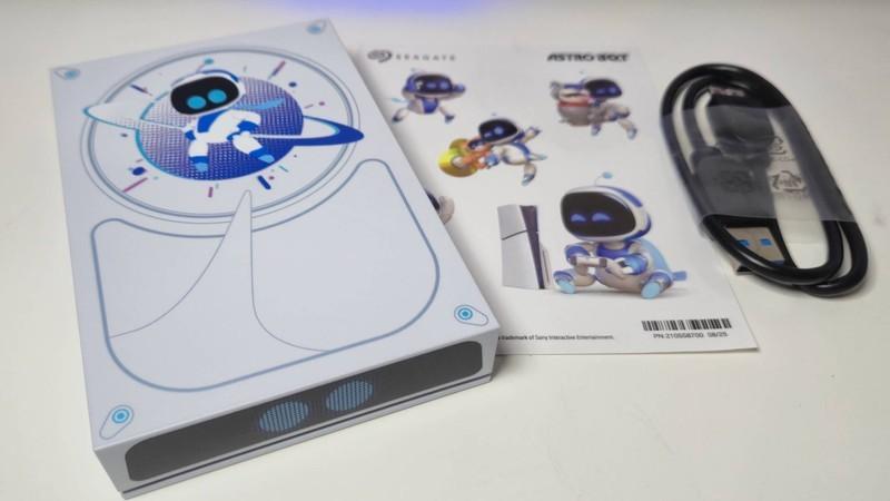Photo of the Astro Bot Seagate drive sitting on a white desk next to a set of stickers and a USB cable.